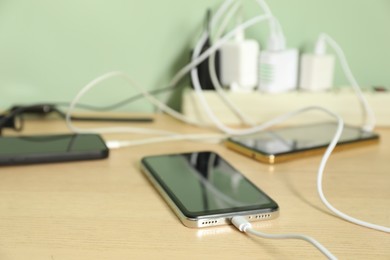 Photo of USB adapters with cables plugged into power strip charging devices on wooden table, closeup