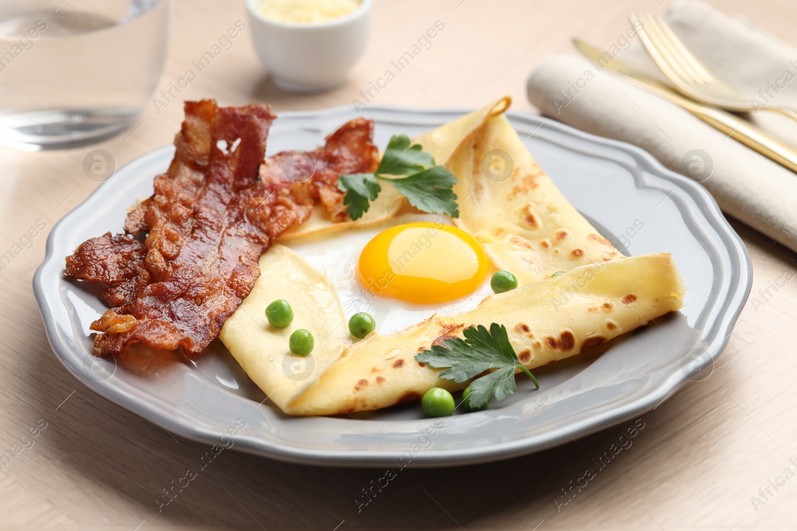 Photo of Delicious crepe with egg, bacon and green peas served on wooden table, closeup. Breton galette