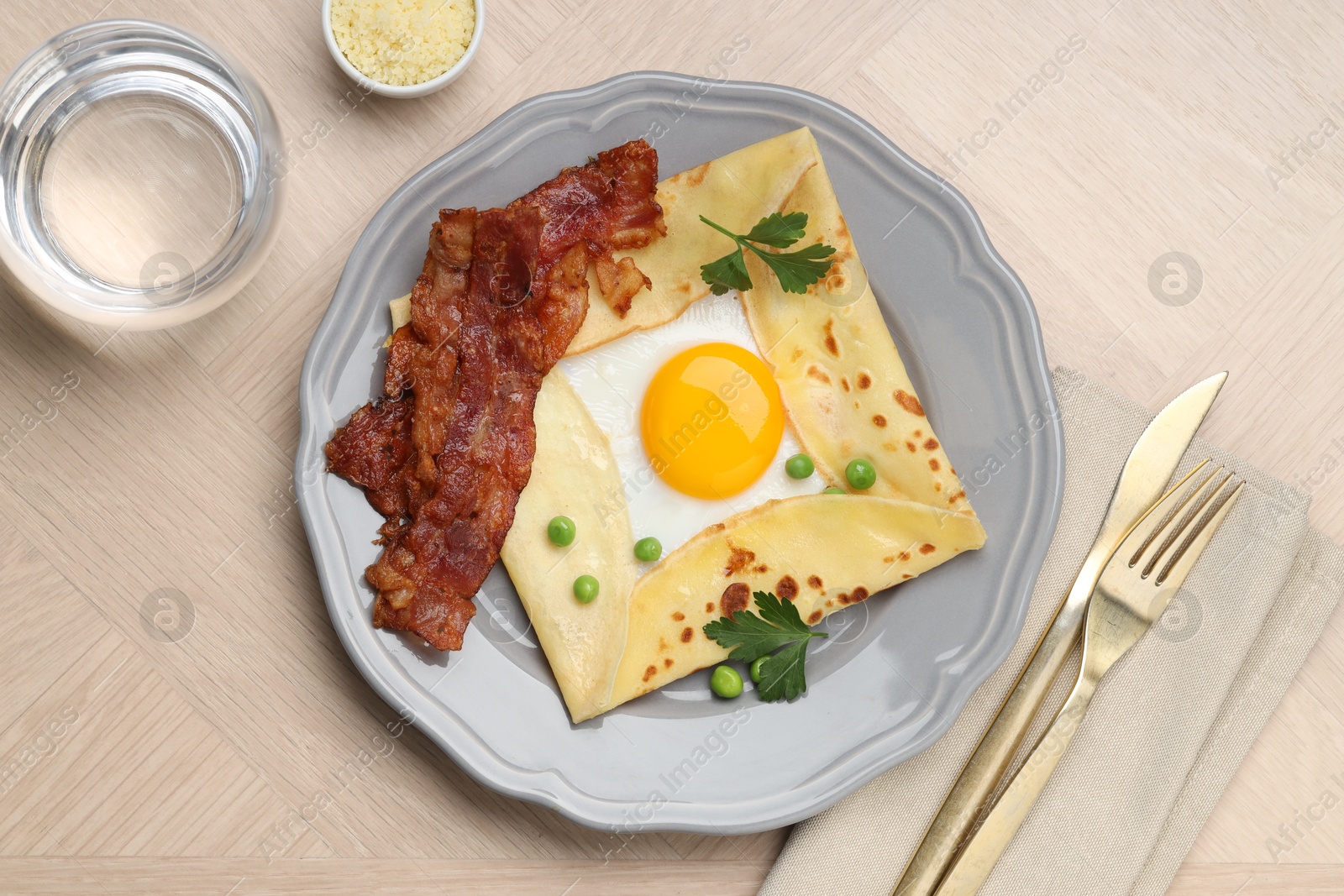 Photo of Delicious crepe with egg, bacon and green peas served on wooden table, flat lay. Breton galette