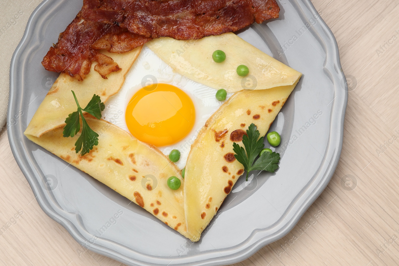 Photo of Delicious crepe with egg, bacon and green peas on wooden table, top view. Breton galette