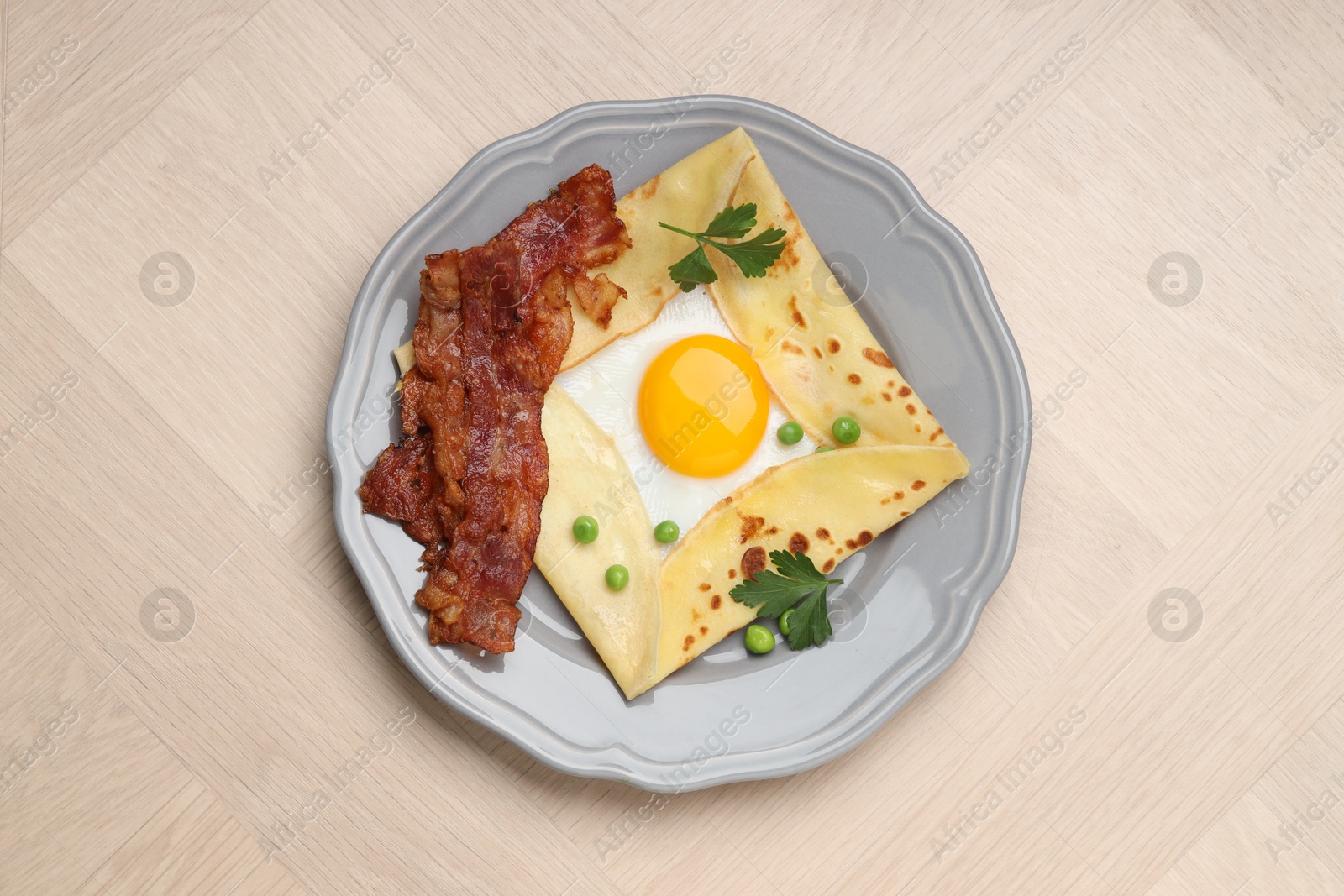 Photo of Delicious crepe with egg, bacon and green peas on wooden table, top view. Breton galette