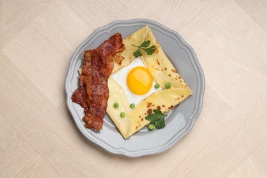 Photo of Delicious crepe with egg, bacon and green peas on wooden table, top view. Breton galette