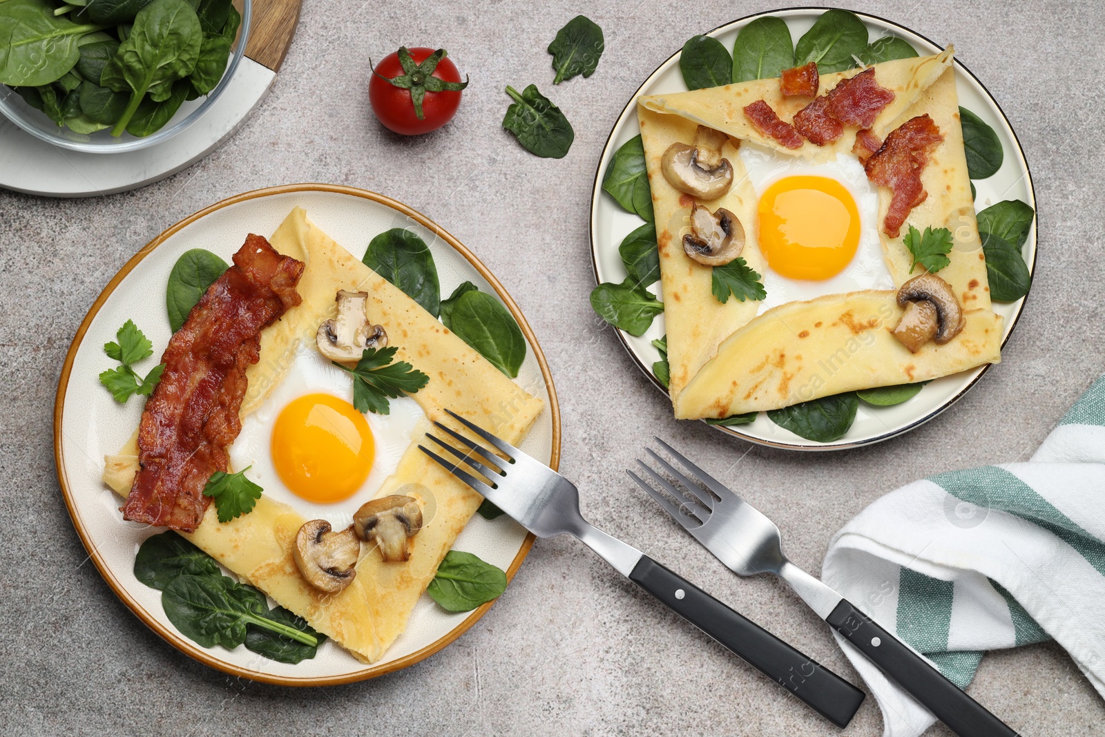 Photo of Delicious crepes with eggs, bacon and mushrooms served on grey table, flat lay. Breton galette