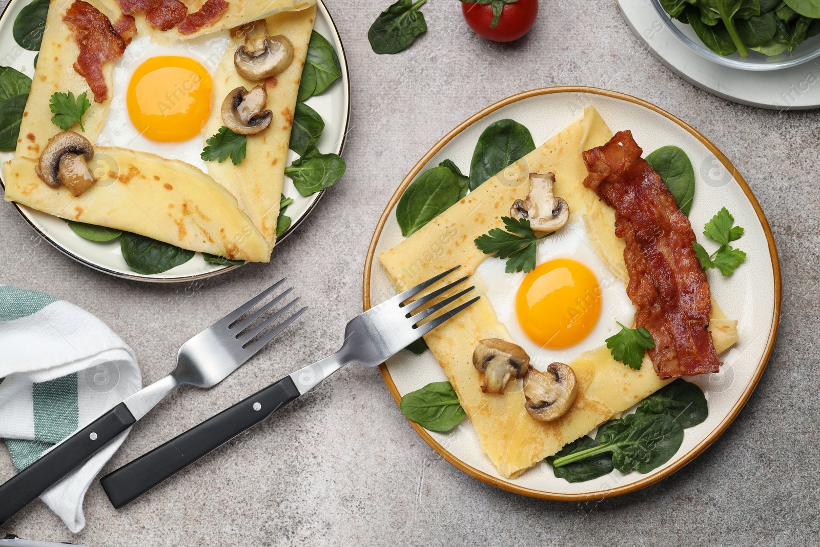 Photo of Delicious crepes with eggs, bacon and mushrooms served on grey table, flat lay. Breton galette