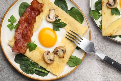 Photo of Delicious crepes with egg, bacon and mushrooms served on grey table, flat lay. Breton galette