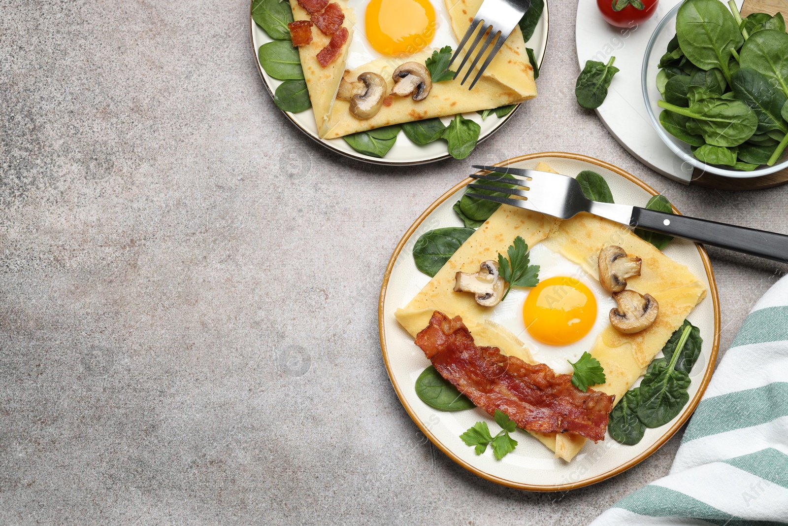 Photo of Delicious crepes with eggs, bacon and mushrooms served on grey table, flat lay. Space for text