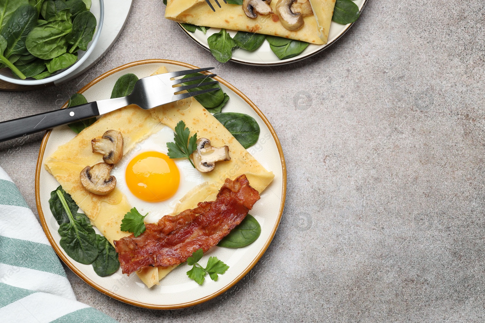 Photo of Delicious crepes with egg, bacon and mushrooms served on grey table, flat lay. Space for text