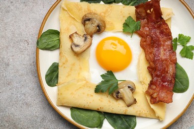 Photo of Delicious crepe with egg, bacon and mushrooms on grey table, top view. Breton galette