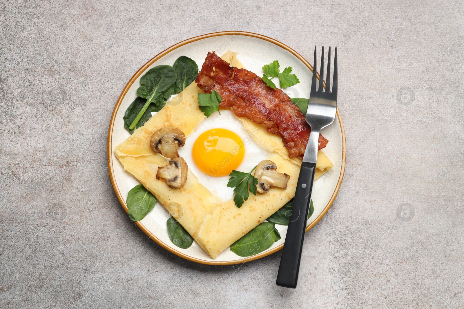 Photo of Delicious crepe with egg, bacon and mushrooms served on grey table, top view. Breton galette