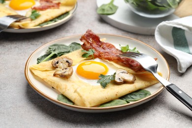 Photo of Delicious crepes with eggs, bacon and mushrooms served on grey table, closeup. Breton galette