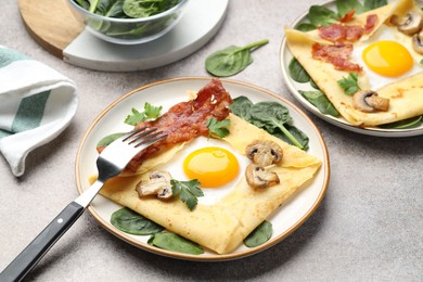 Photo of Delicious crepes with eggs, bacon and mushrooms served on grey table, closeup. Breton galette