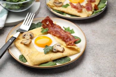 Photo of Delicious crepes with eggs, bacon and mushrooms served on grey table, closeup. Breton galette