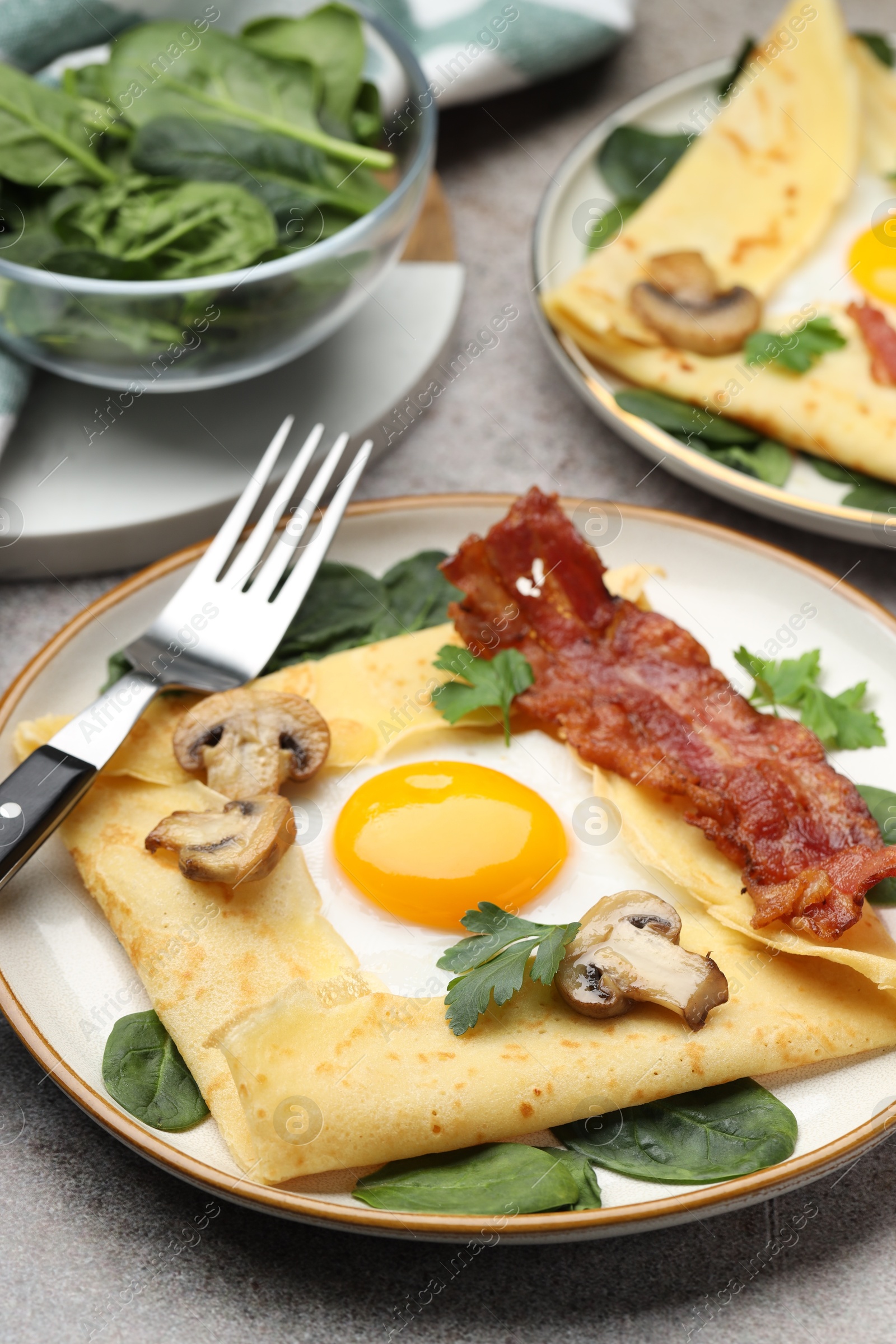 Photo of Delicious crepes with eggs, bacon and mushrooms served on grey table, closeup. Breton galette