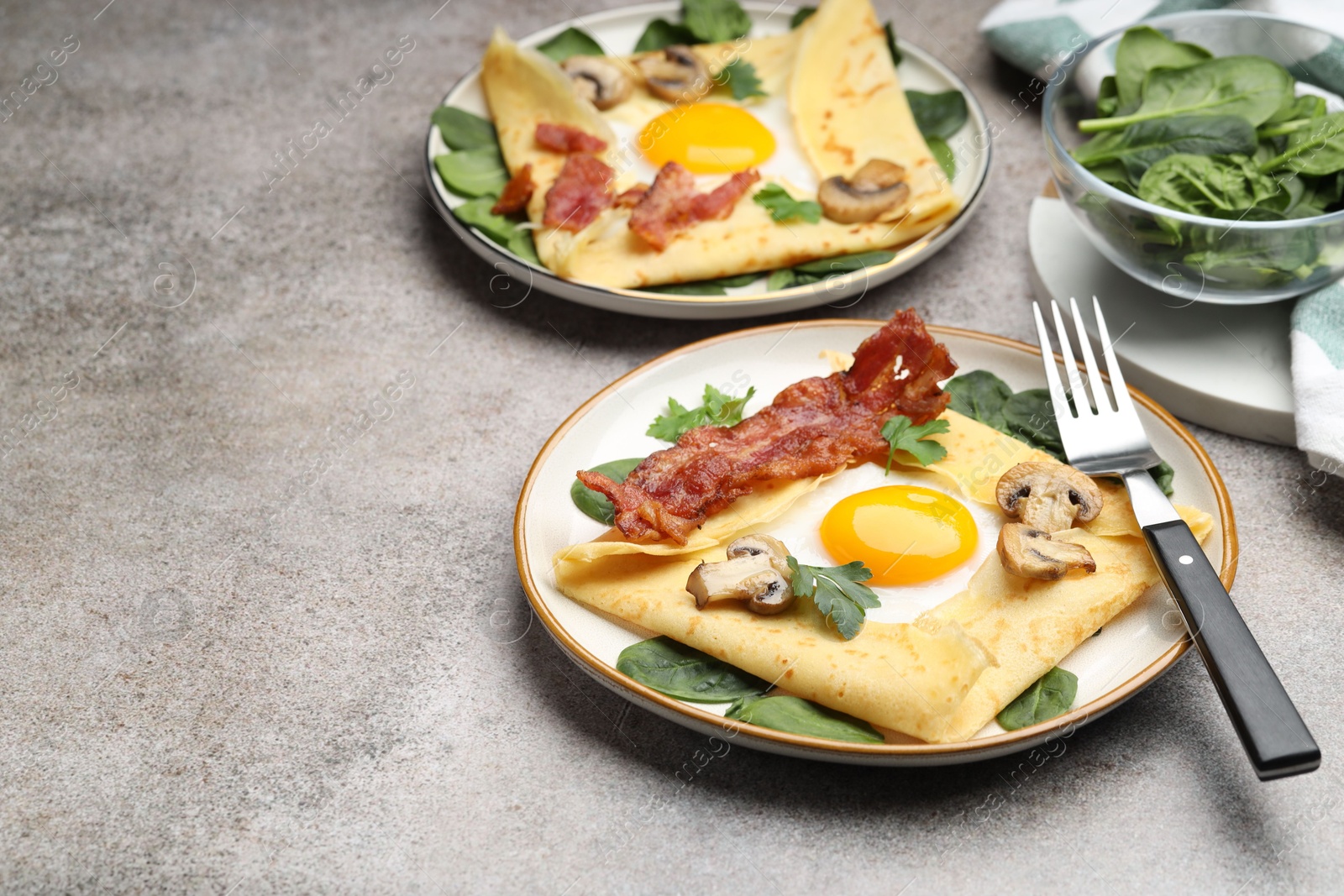 Photo of Delicious crepes with eggs, bacon and mushrooms served on grey table, closeup. Space for text