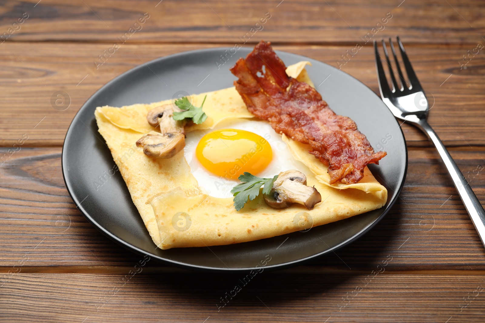 Photo of Delicious crepe with egg, bacon and mushrooms served on wooden table, closeup. Breton galette