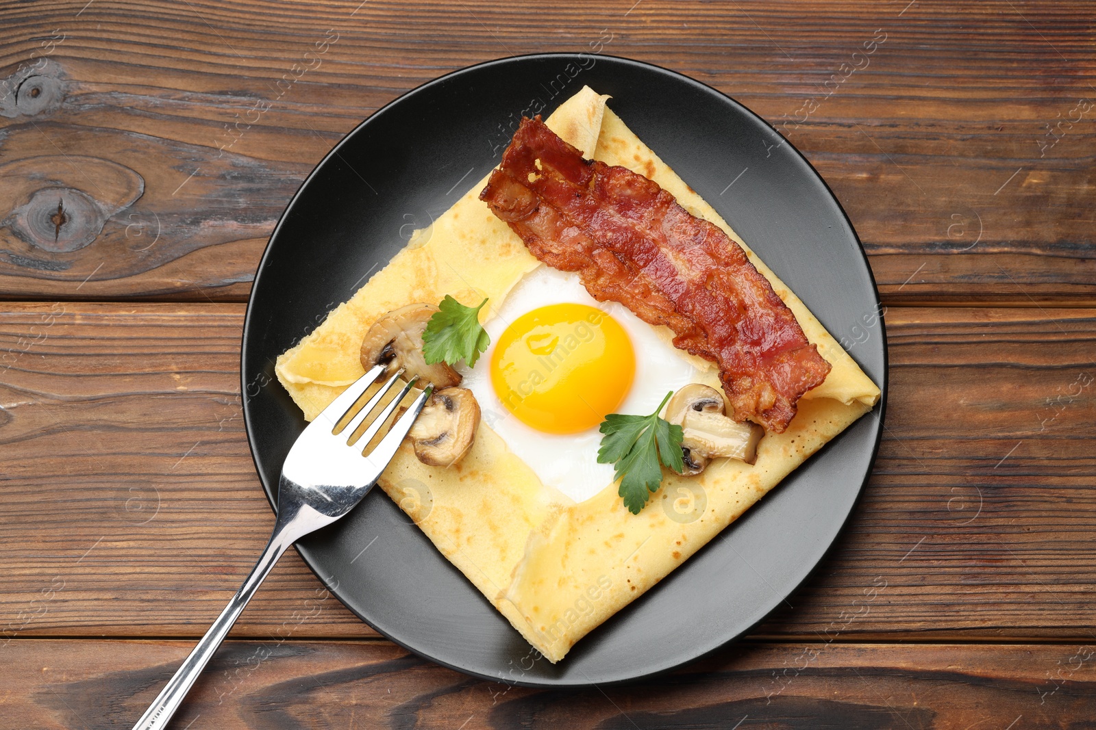 Photo of Delicious crepe with egg, bacon and mushrooms served on wooden table, top view. Breton galette