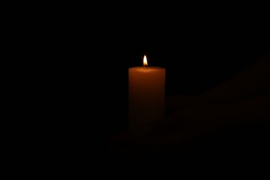 Photo of One burning church candle on dark background