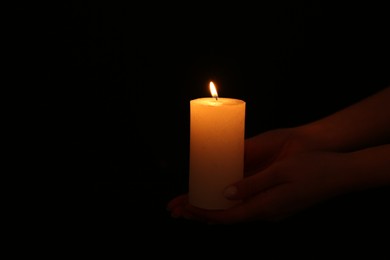 Photo of Woman with burning candle on dark background, closeup. Space for text