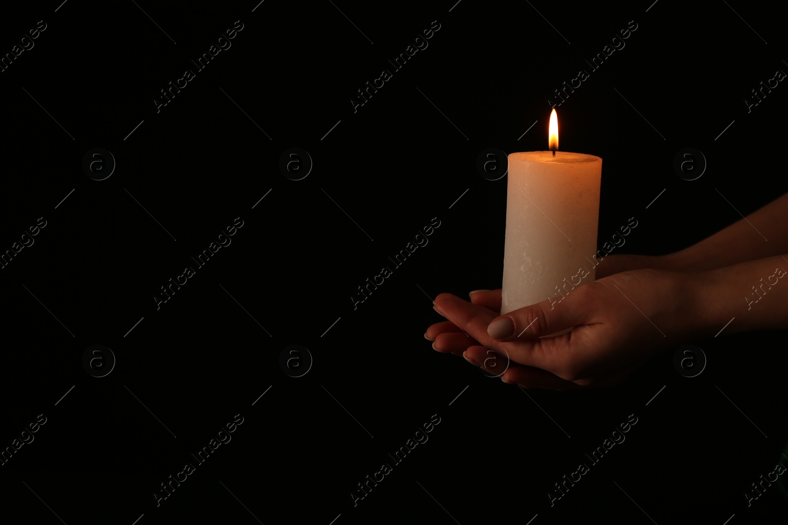 Photo of Woman with burning candle on dark background, closeup. Space for text