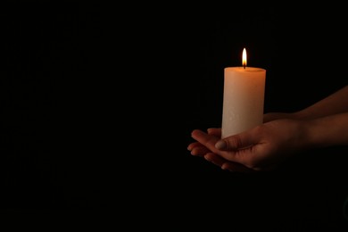 Photo of Woman with burning candle on dark background, closeup. Space for text