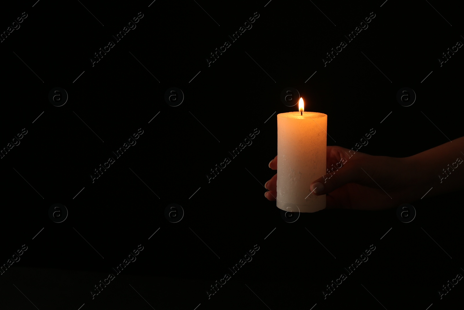 Photo of Woman with burning candle on dark background, closeup. Space for text