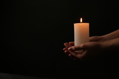 Photo of Woman with burning candle on dark background, closeup. Space for text