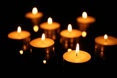 Photo of Many burning candles on dark background, closeup