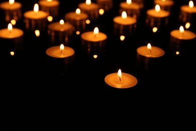 Photo of Many burning candles on dark background, closeup