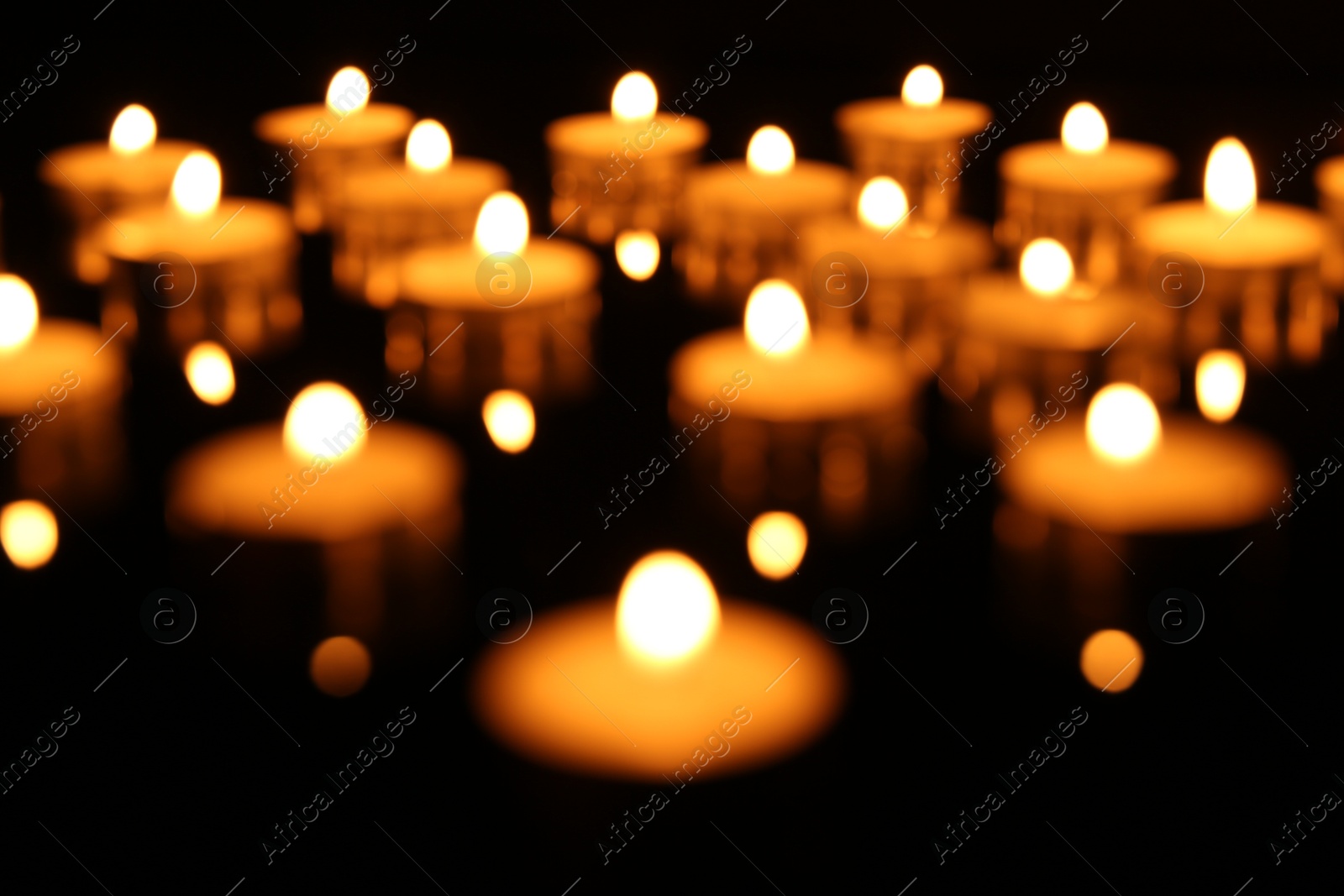 Photo of Blurred view of many burning candles on dark background, closeup