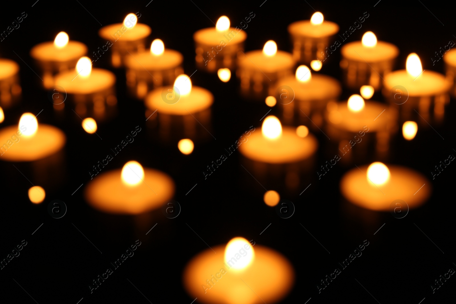 Photo of Blurred view of many burning candles on dark background, closeup