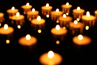 Photo of Blurred view of many burning candles on dark background, closeup