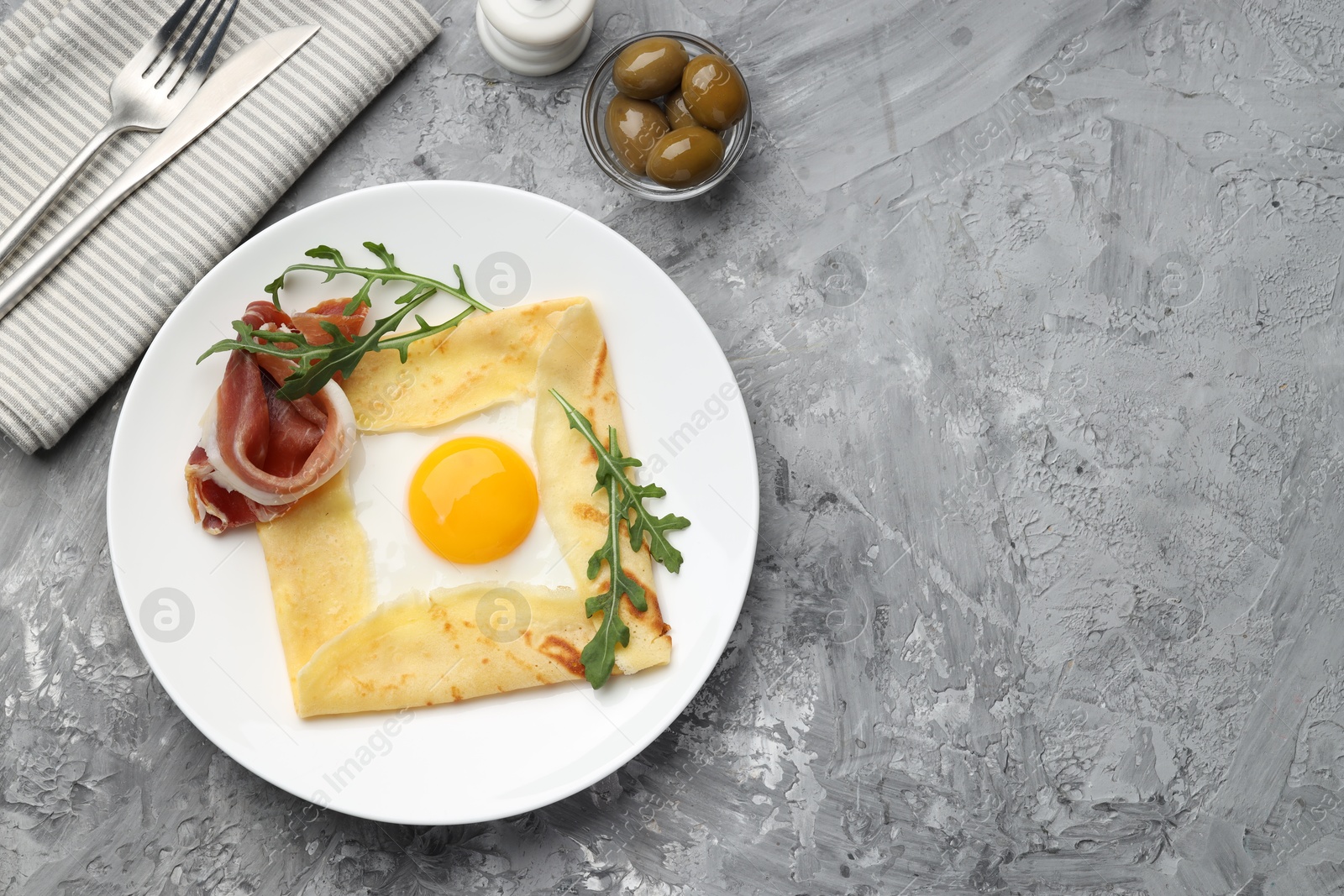 Photo of Delicious crepe bretonne with bacon and arugula served on grey textured table, flat lay. Space for text