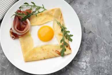 Photo of Delicious crepe bretonne with bacon and arugula on grey textured table, top view