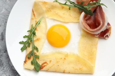 Photo of Delicious crepe bretonne with bacon and arugula on grey textured table, top view