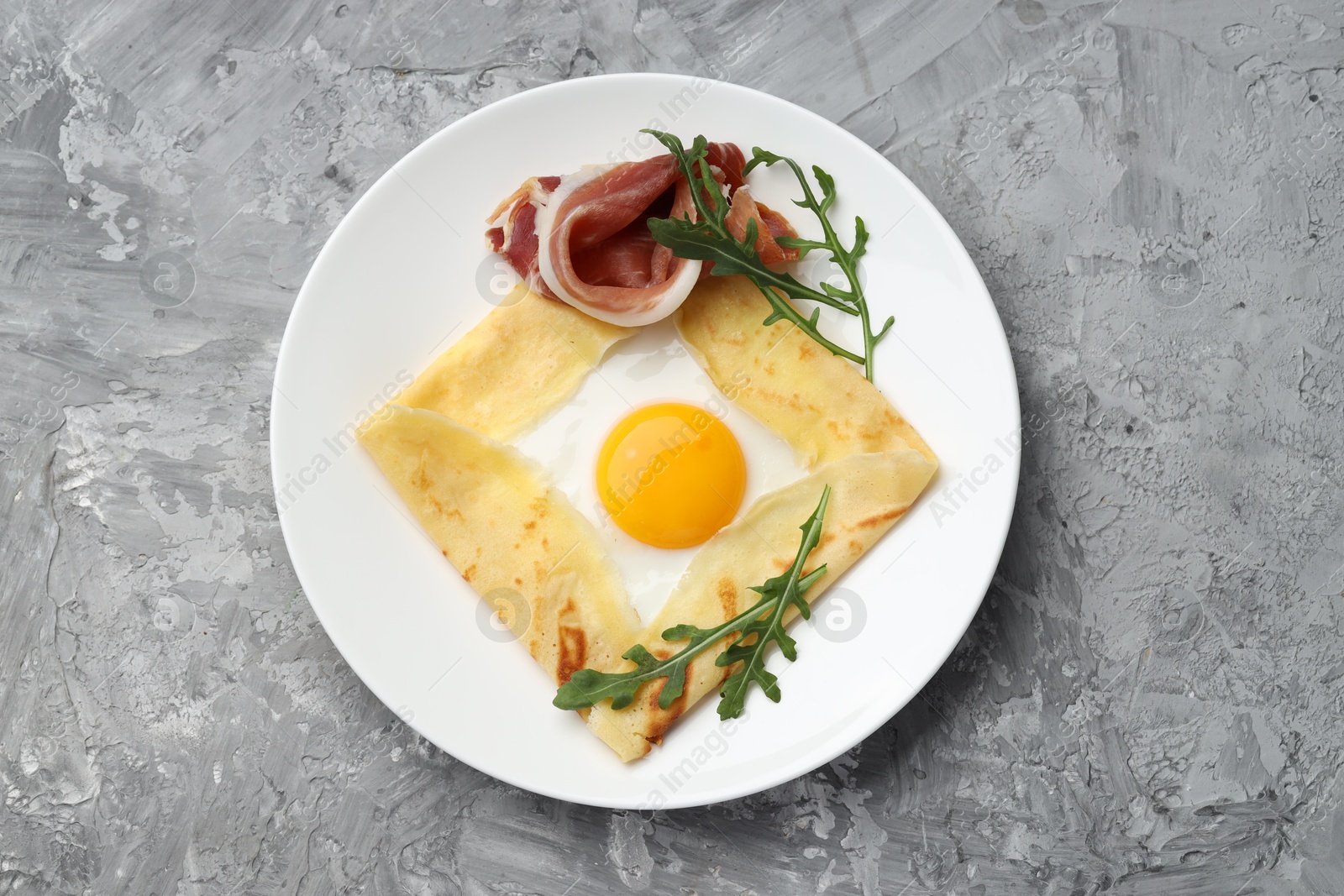 Photo of Delicious crepe bretonne with bacon and arugula on grey textured table, top view