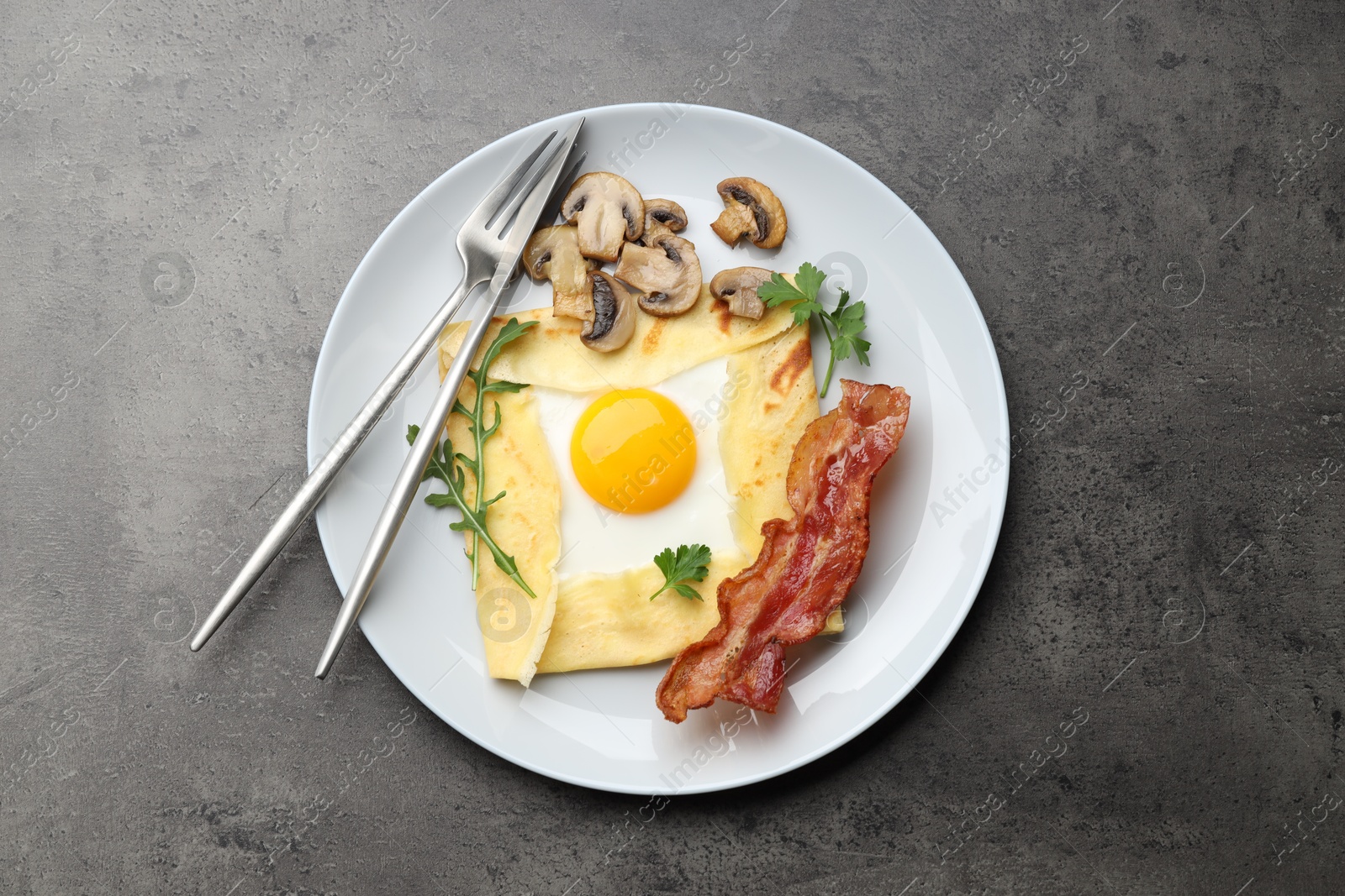 Photo of Delicious crepe bretonne with bacon, mushrooms and arugula served on grey table, top view