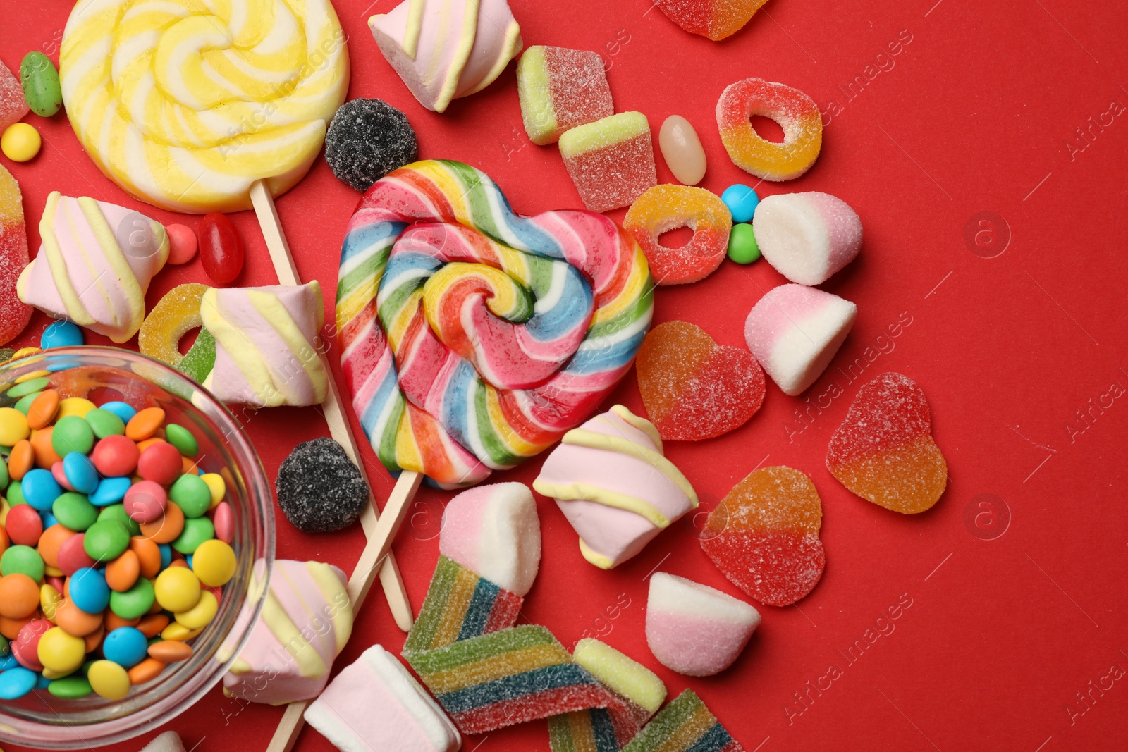 Photo of Different delicious candies and marshmallows on red background, flat lay