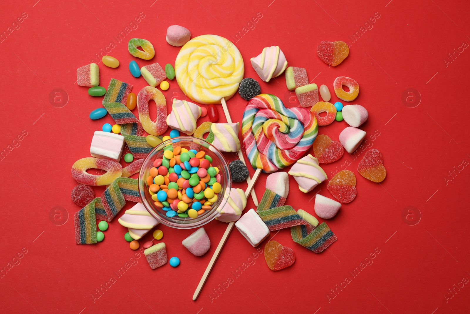 Photo of Different delicious candies and marshmallows on red background, flat lay