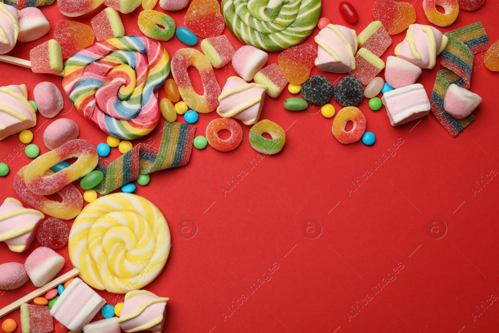 Photo of Different delicious candies and marshmallows on red background, flat lay. Space for text