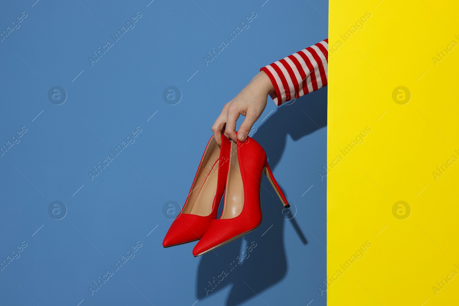 Photo of Woman showing red high-heeled shoes on color background, closeup. Stylish presentation