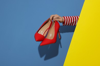 Photo of Woman showing red high-heeled shoes on color background, closeup. Stylish presentation