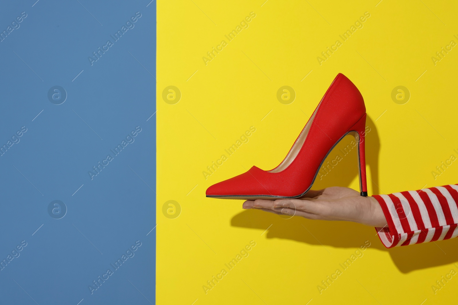 Photo of Woman showing red high-heeled shoe on color background, closeup and space for text. Stylish presentation