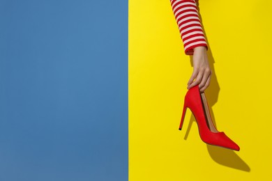 Photo of Woman showing red high-heeled shoe on color background, closeup and space for text. Stylish presentation