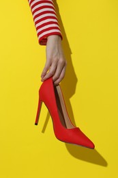 Photo of Woman showing red high-heeled shoe on yellow background, closeup