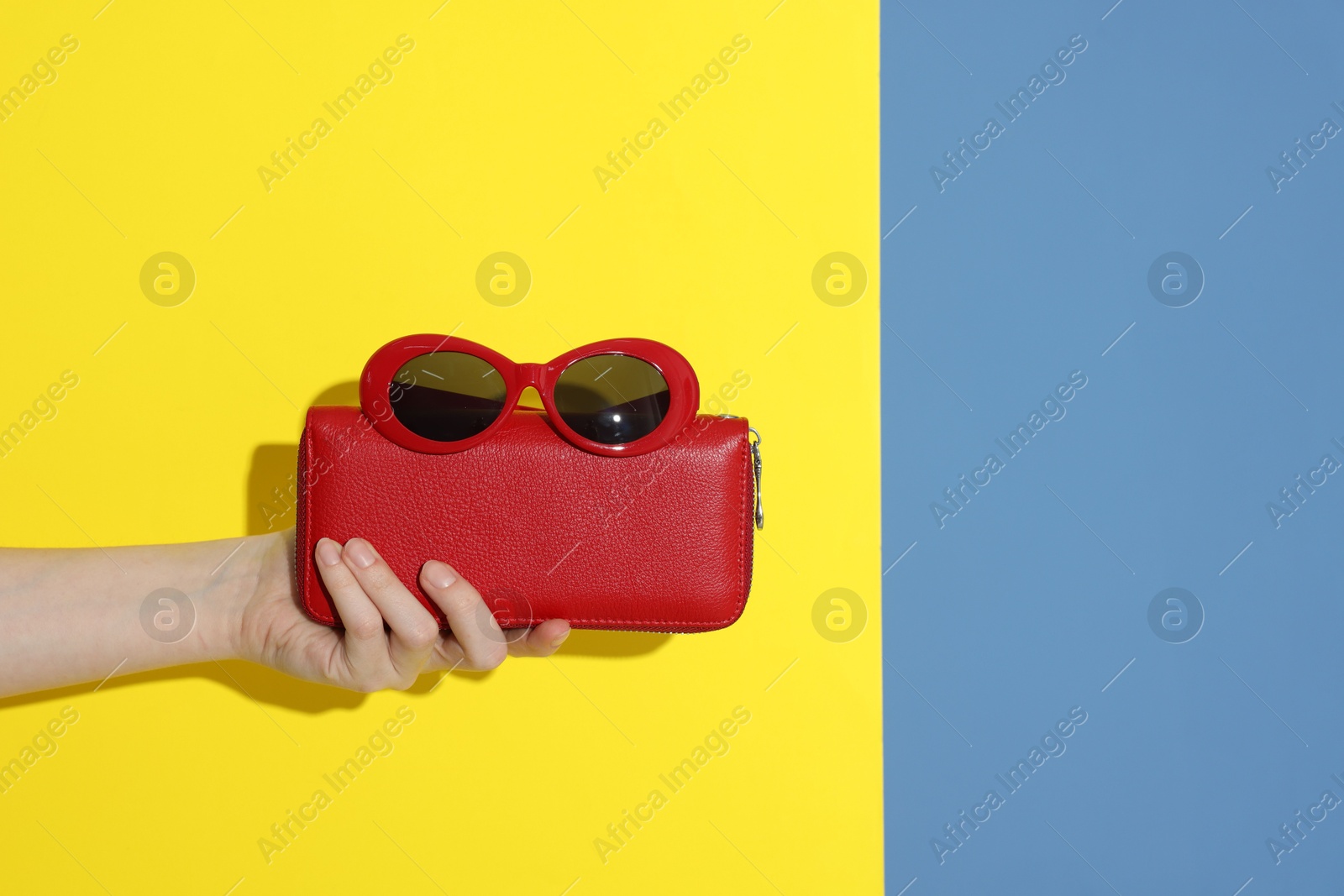 Photo of Woman showing red wallet and sunglasses on color background, closeup with space for text. Stylish presentation