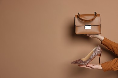 Photo of Woman showing stylish bag and glitter high-heeled shoe on beige background, closeup. Space for text