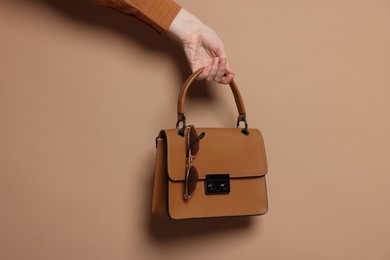 Photo of Woman showing stylish handbag and sunglasses on beige background, closeup