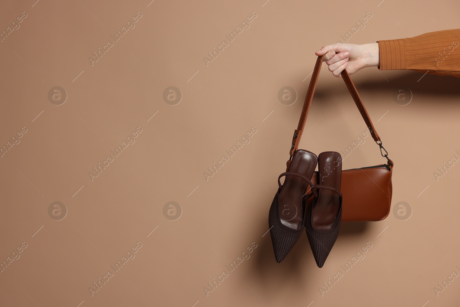 Photo of Woman showing stylish handbag and high-heeled shoes on beige background, closeup. Space for text