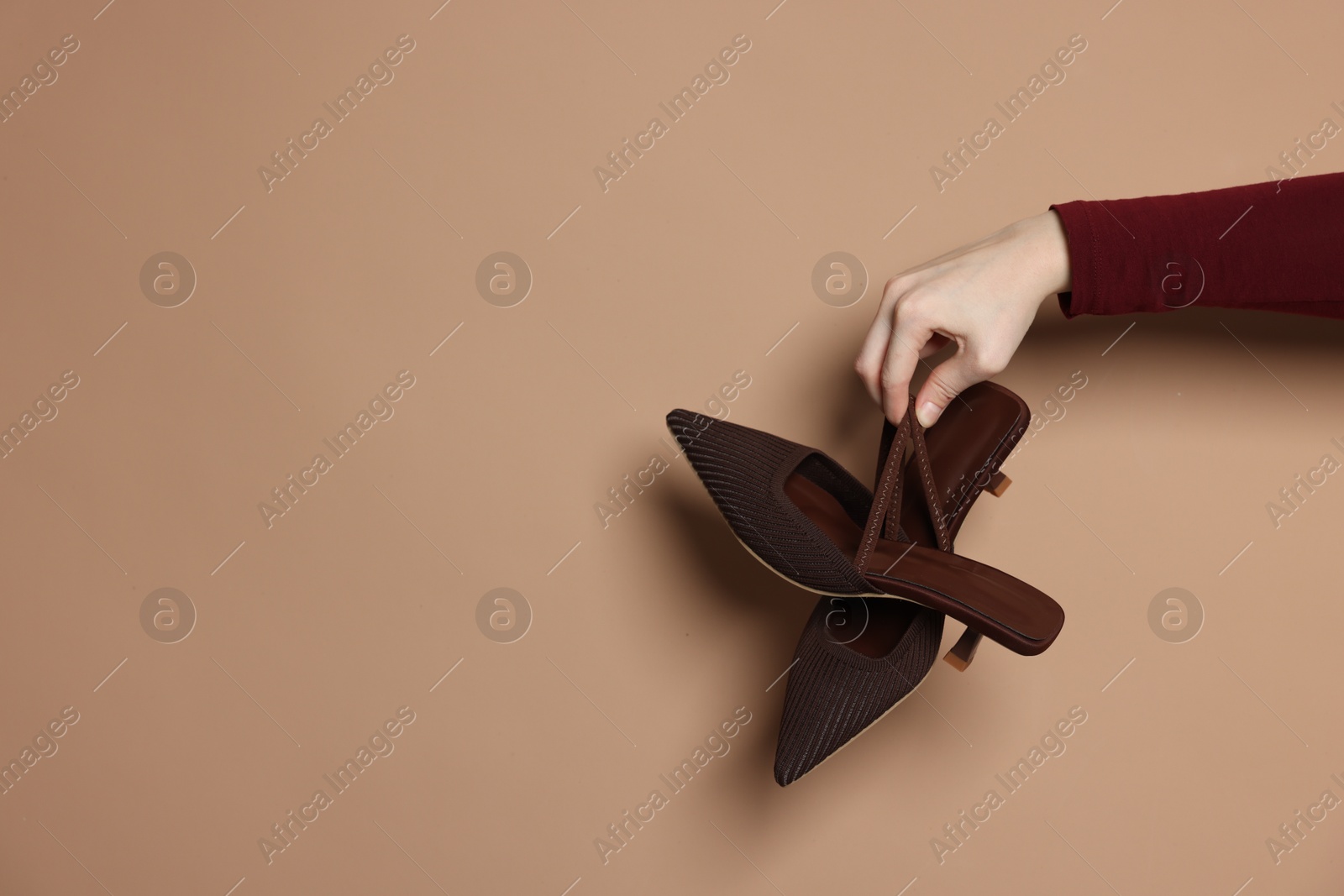 Photo of Woman showing stylish high-heeled shoes on beige background, closeup. Space for text