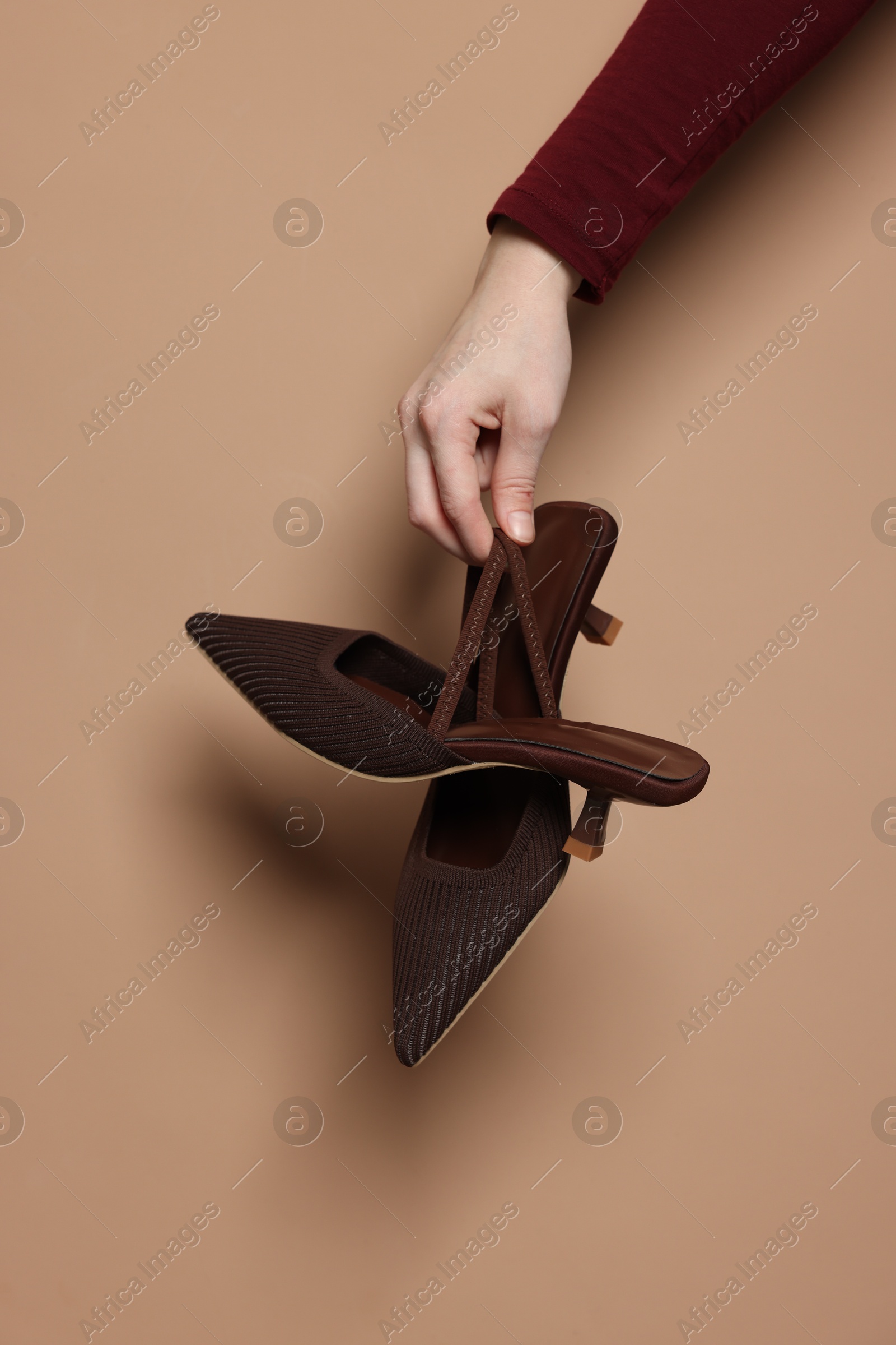 Photo of Woman showing stylish high-heeled shoes on beige background, closeup